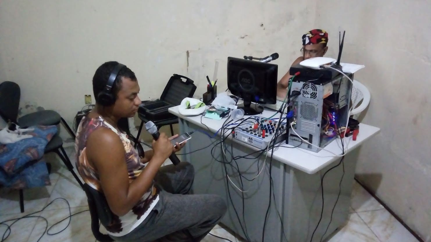 Locutor de fones de ouvido falando ao microfone no estúdio da rádio, ao lado de computador e mesa de som