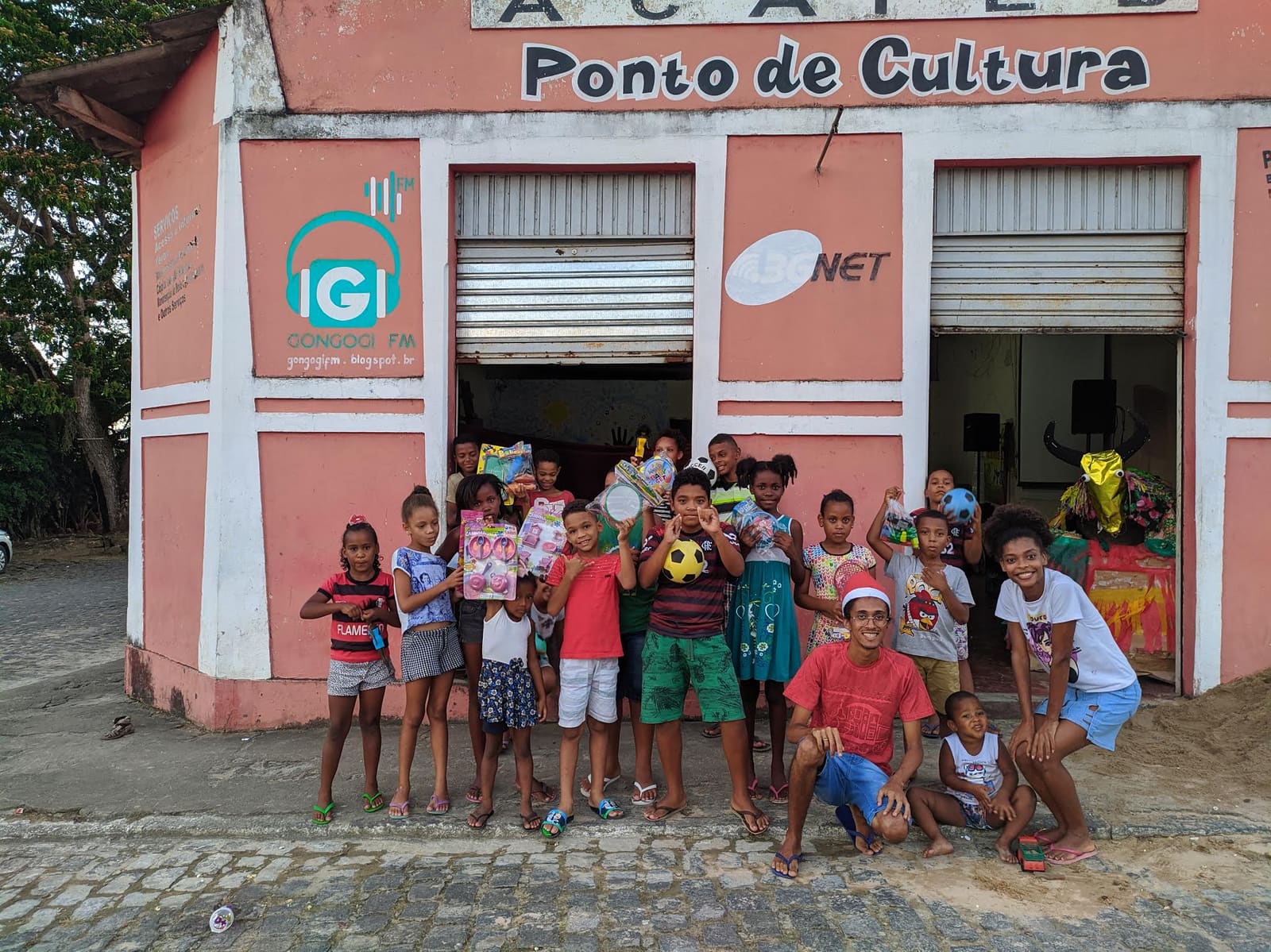 Crianças e educadores da ACAPEB em frente à sede, uma casa rosa com o letreiro Ponto de Cultura, em Gongogi.
